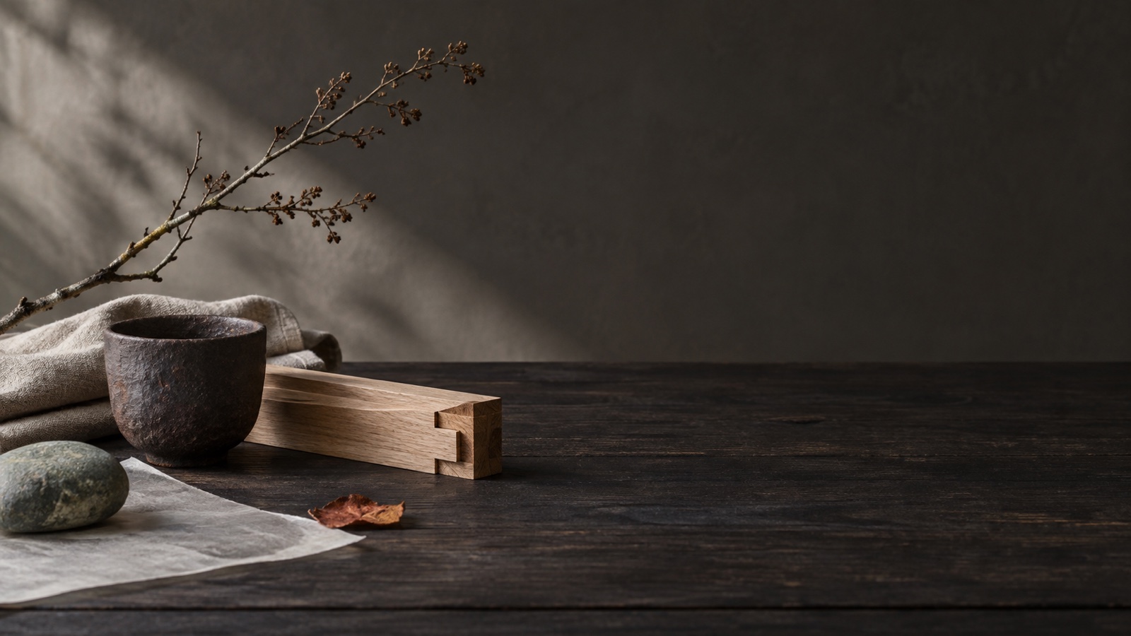 Japandi material still life with pale oak joinery, dark handmade ceramic, linen, paper, stone, and an asymmetrical branch